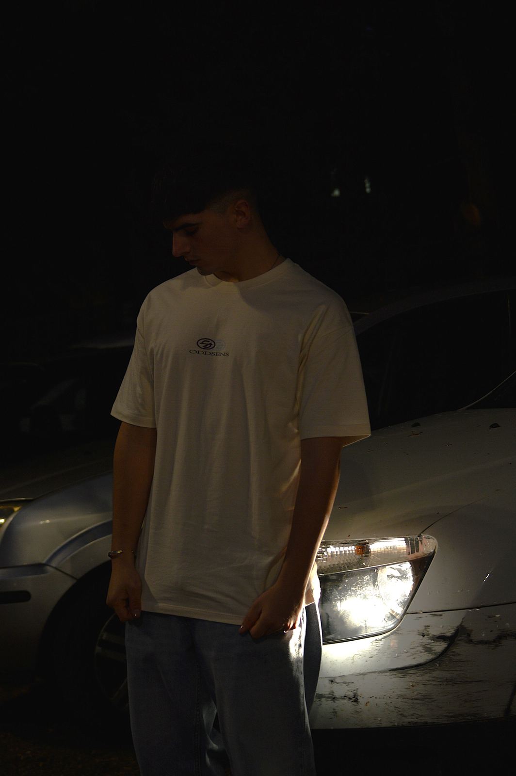 Modelo de noche con la camiseta Logo junto al faro de un coche